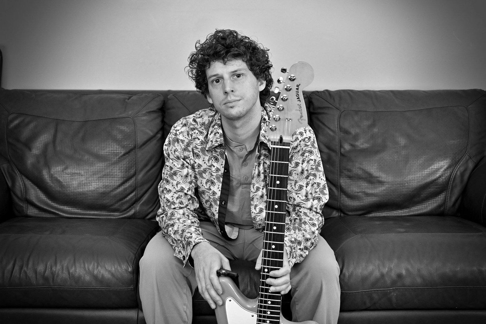 Black and white portrait of Austin Finnegan with a guitar on a couch
